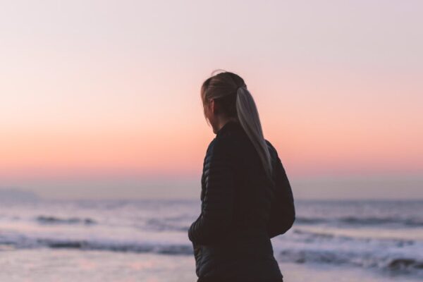 A woman walks along the beach at sunset, enjoying the tranquil ocean scenery.