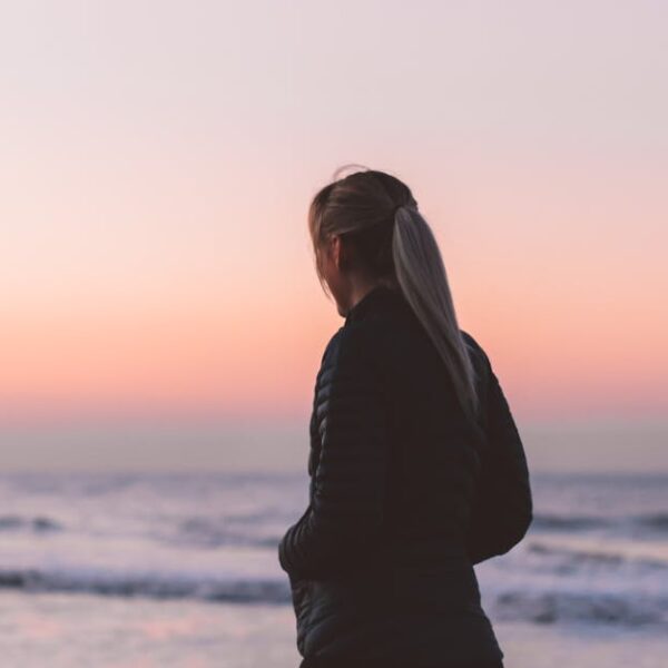 A woman walks along the beach at sunset, enjoying the tranquil ocean scenery.